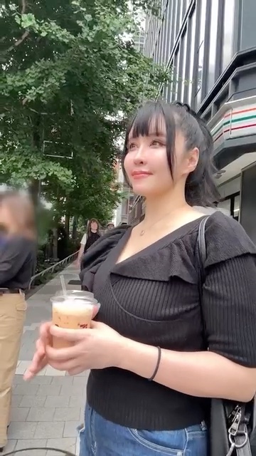 ビル街の交差点でアイスコーヒーを持って笑うKカップの人妻